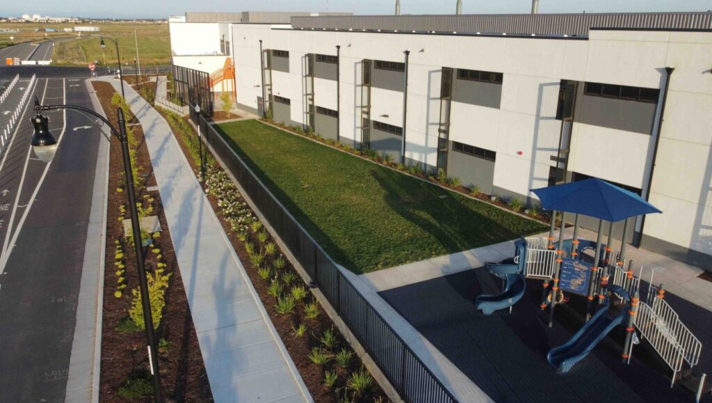 Modern industrial building with green landscaping and a paved walkway.